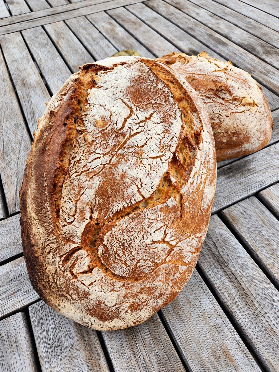 Deux miches de pain de campagne à la croûte dorée et farinée posées sur une table en bois patiné.